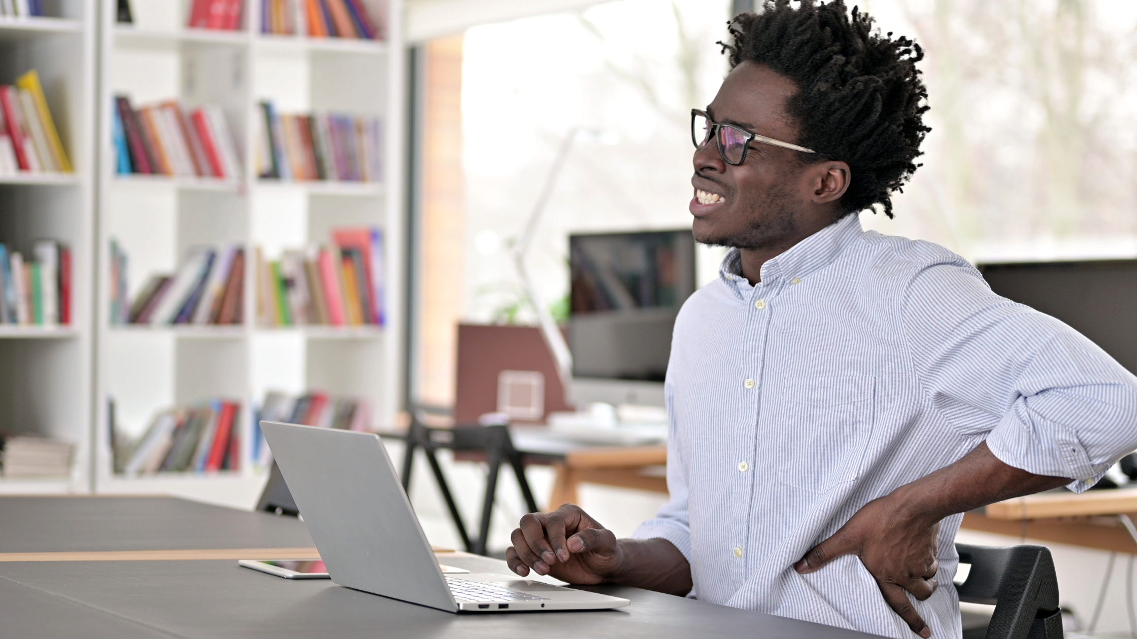 young man with back pain at work sitting at desk